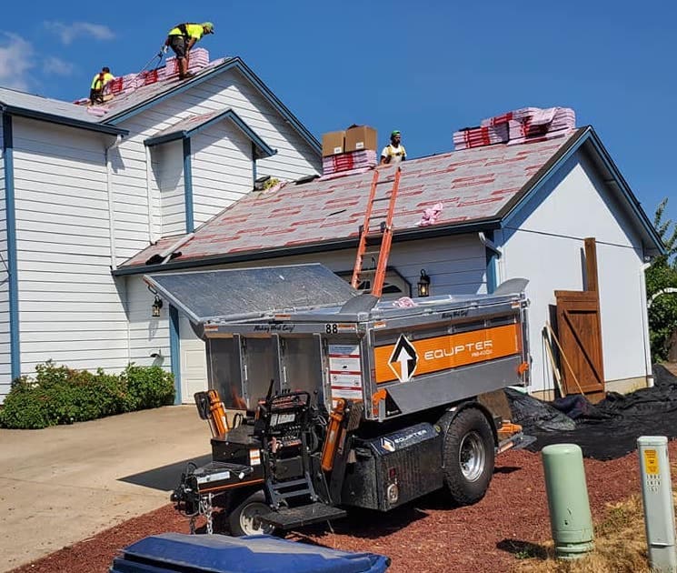 Workers installing a new roof on a home with equipment and materials visible.