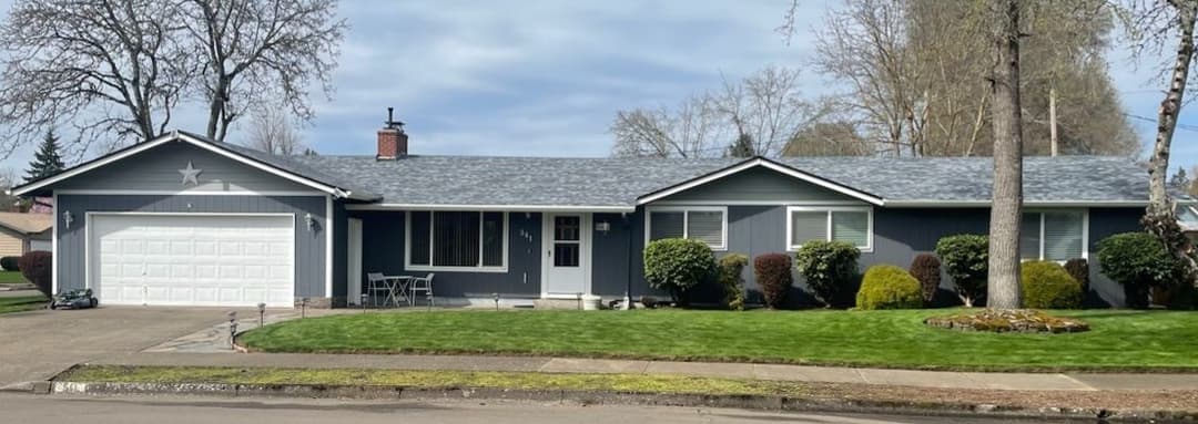 Single-story gray house with a star accent, manicured lawn, and a garage on a residential street.