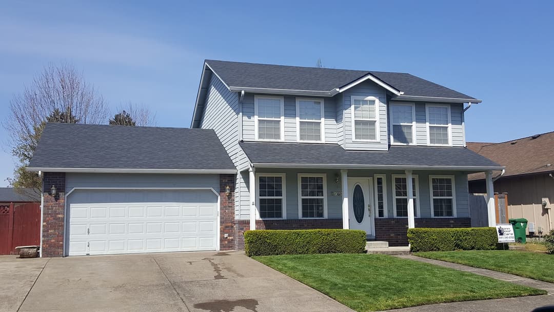 Two-story suburban home with a manicured lawn, attached garage, and clear blue sky.