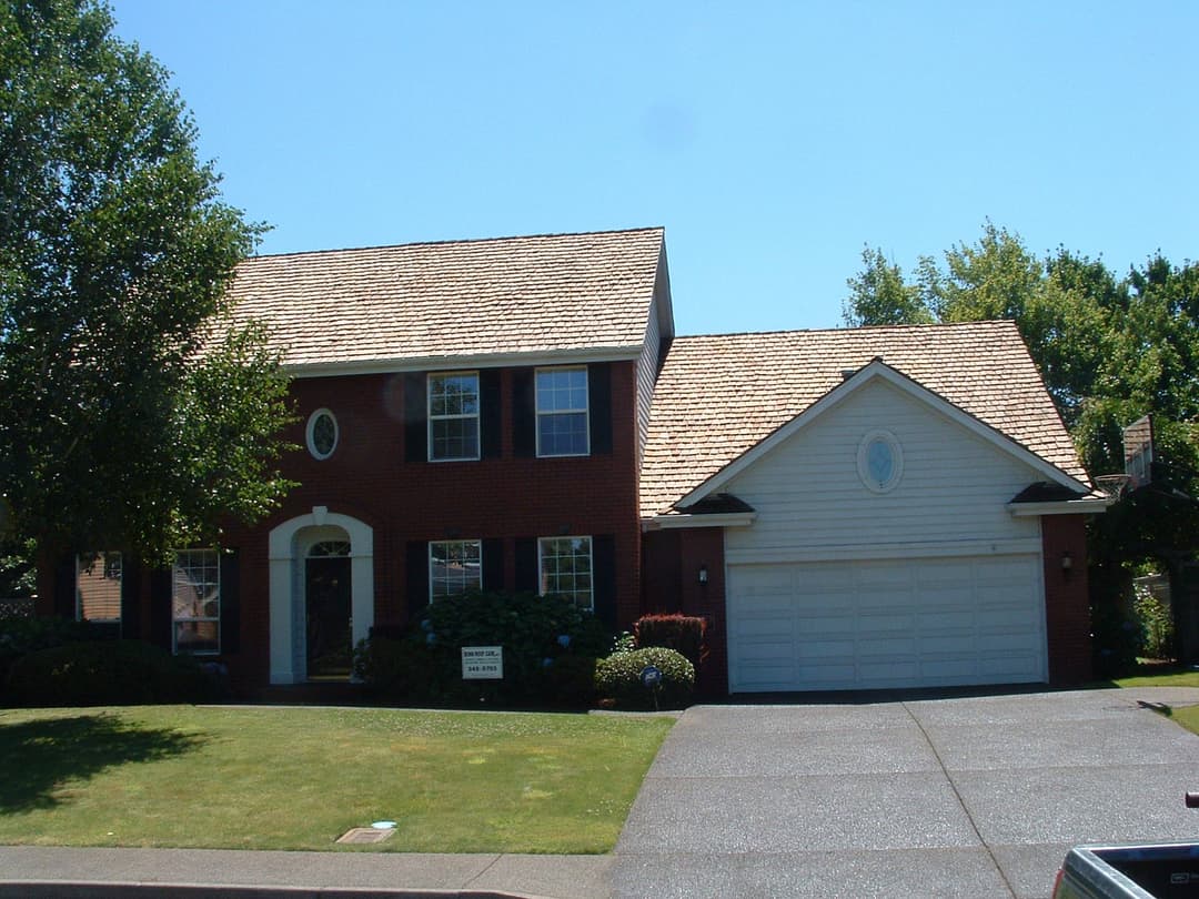 Two-story red brick house with a brown shingle roof and a manicured lawn.