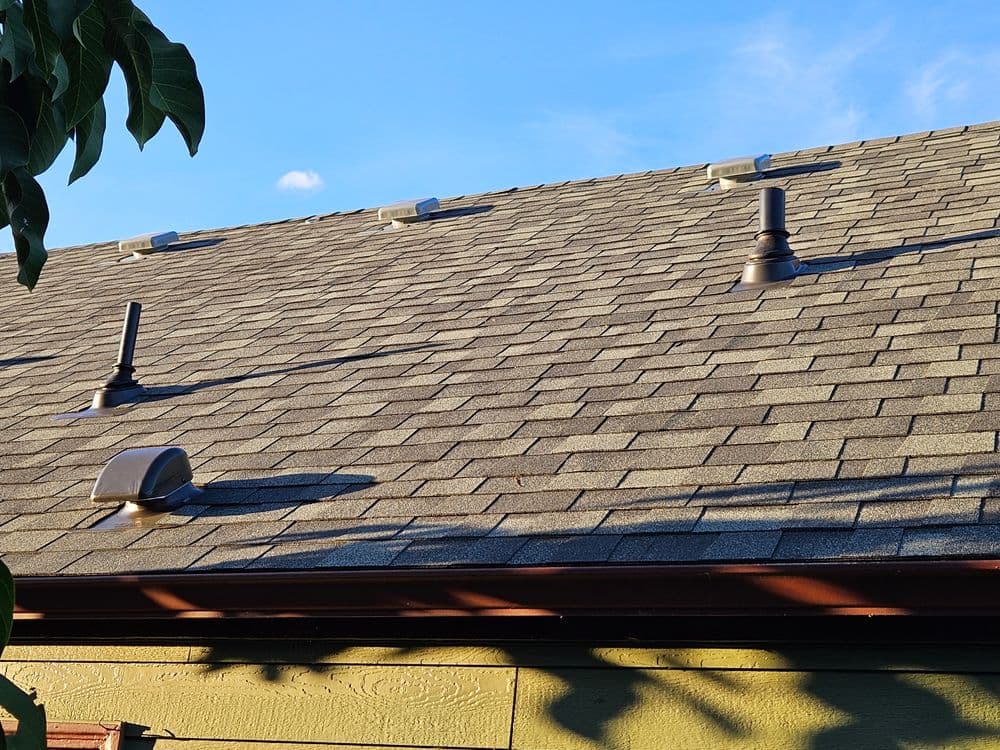 Roof with asphalt shingles, vents, and clear blue sky in the background.