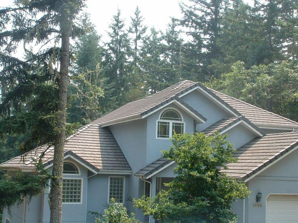 Modern grey house among tall trees with a sloped roof and large arched window.