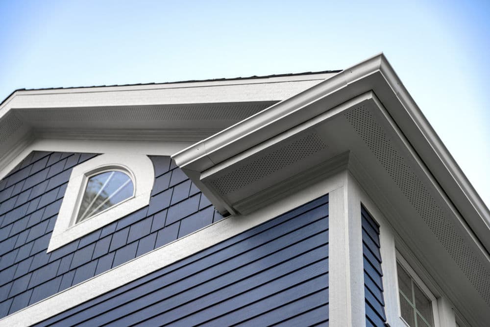 Blue house exterior with detailed trim and roofing against a clear sky.